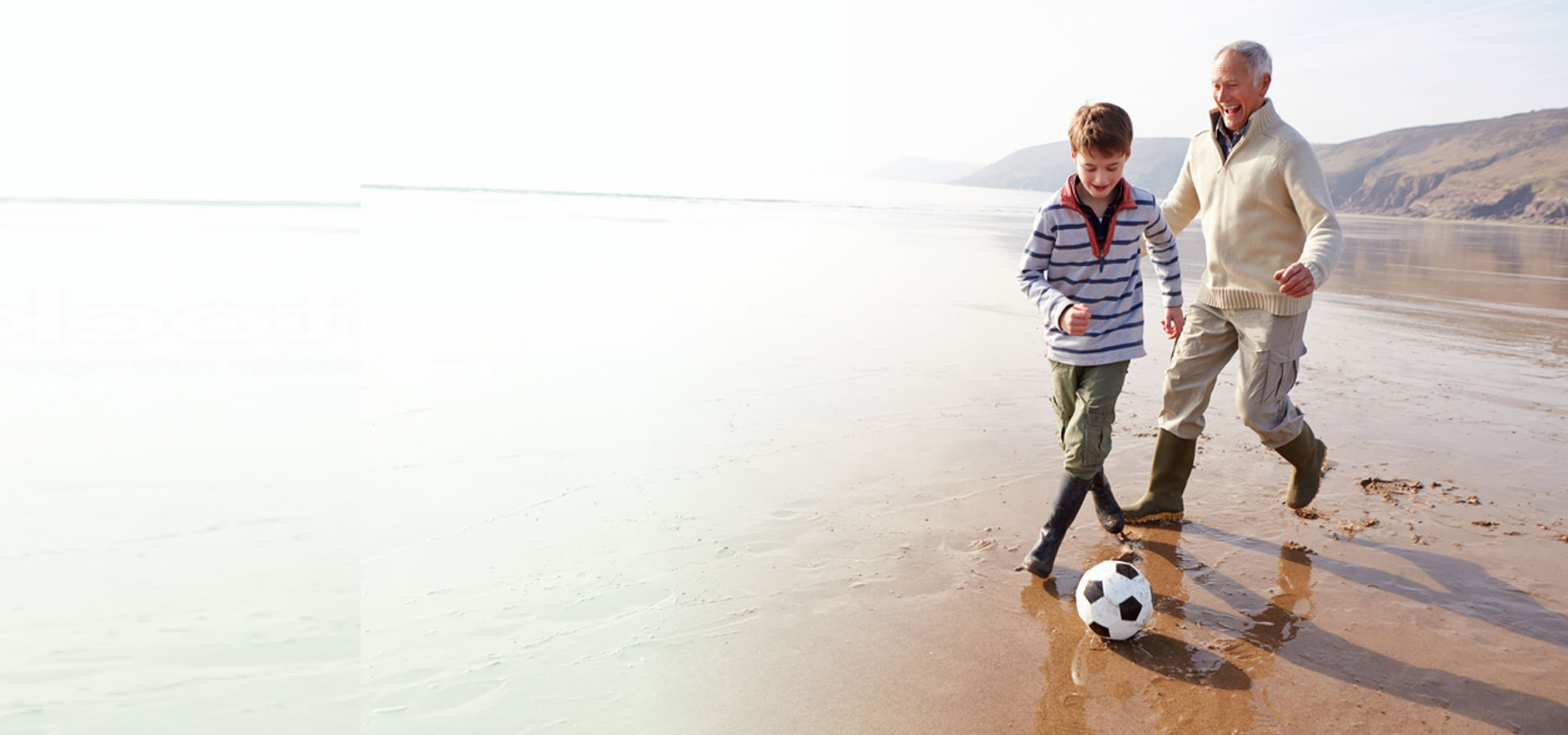 Happy grandfather and son playing soccer on the beach